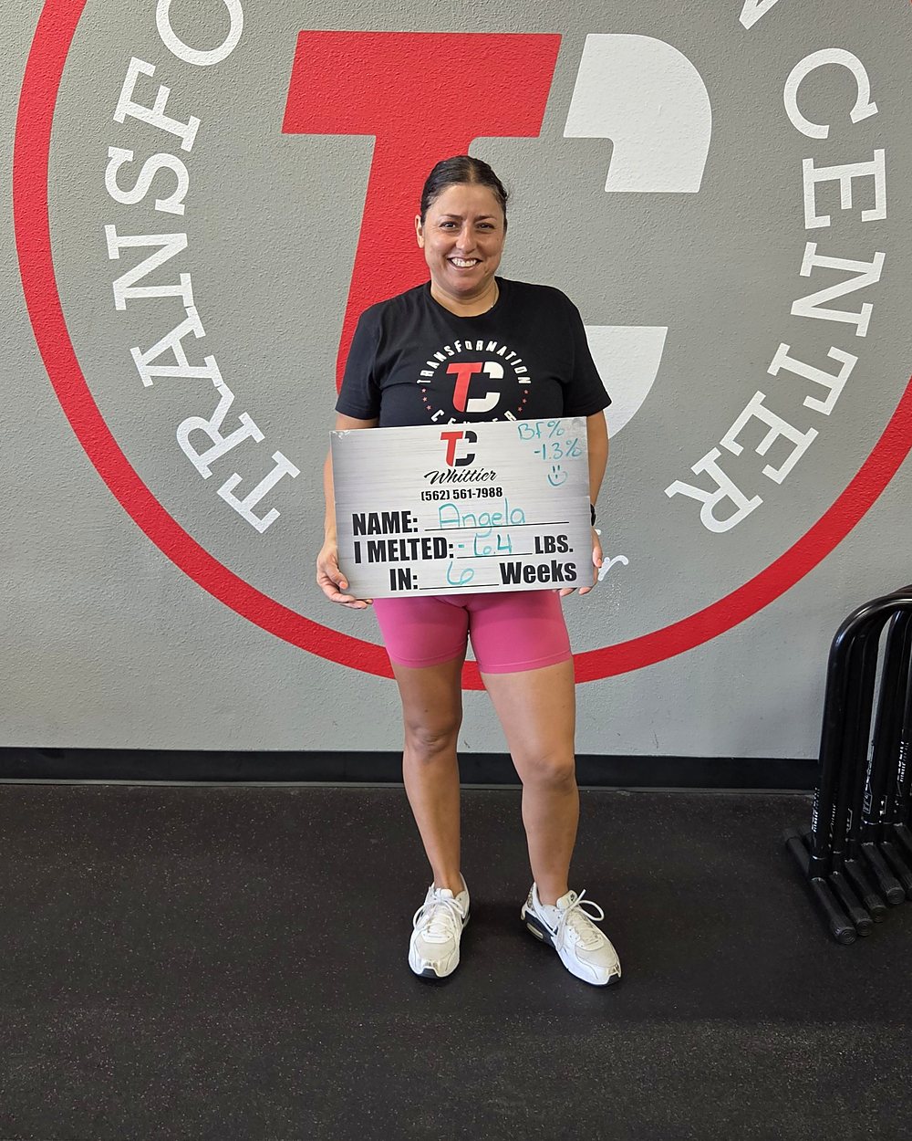 Angela at a Camp Whittier weigh-in, holding a board that reads: melted 6.4 pounds in 6 weeks, with body fat down 1.3 percent.