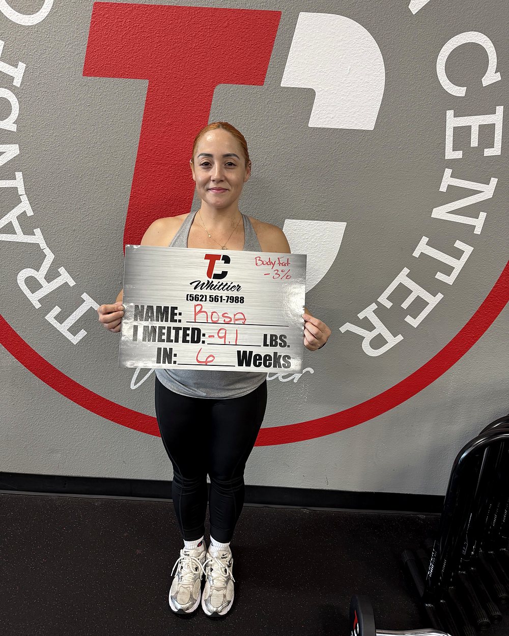Rosa at a Camp Whittier weigh-in, holding a board that reads: melted 9.1 pounds in 6 weeks, with body fat down 3 percent.