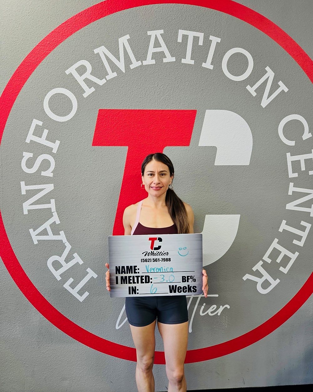 Veronica at a Camp Whittier weigh-in, holding a board that reads: melted 3 percent body fat in 6 weeks.