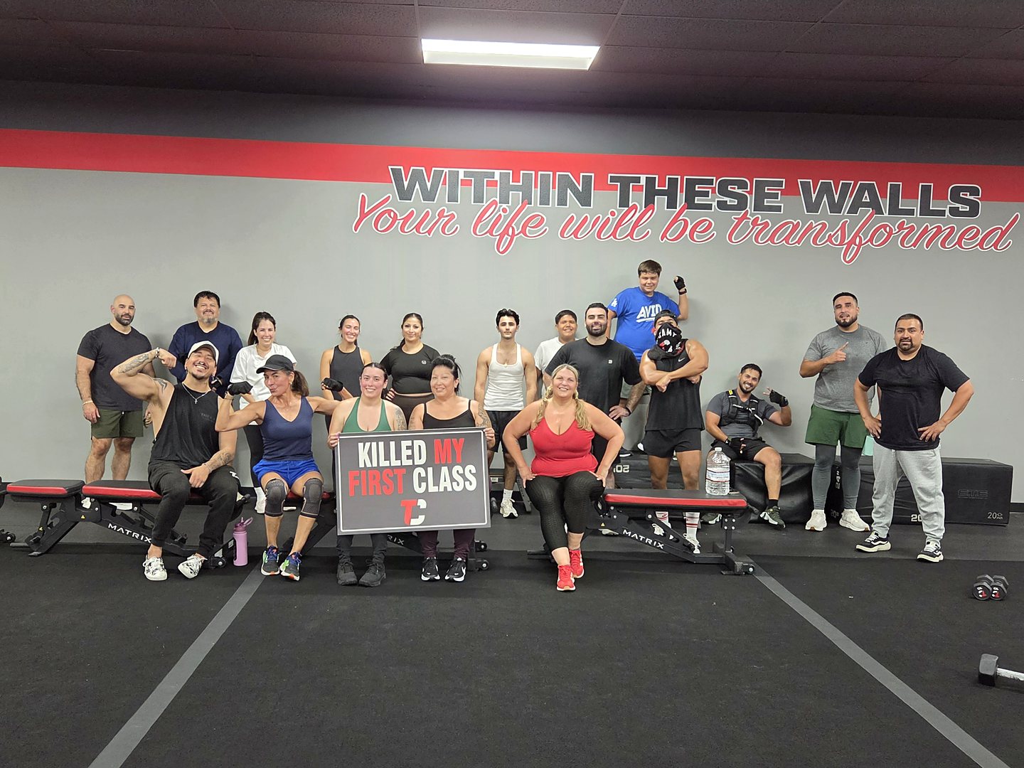 A Camp Whittier class on the benches under the &ldquo;Within these walls, your life will be transformed&rdquo; mural, holding a &ldquo;Killed my first class&rdquo; sign.